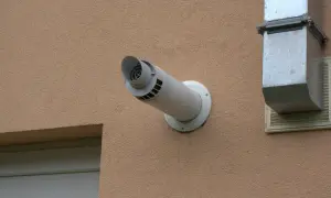 Odprowadzenie spalin z pieca gazowego przez ścianę, zgodnie z przepisami, wymaga odpowiedniej instalacji. Widoczny biały kominek wentylacyjny i metalowy kanał.