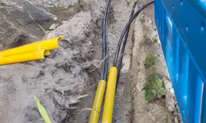 Kable elektryczne w żółtych osłonach w wykopie. Trudno określić na jakiej głębokości kabel elektryczny, ale widać jego zabezpieczenie.