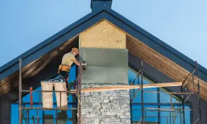 Pracownik montuje izolację na kominie, który będzie wykończony kamieniem. Różne rodzaje kominów wymagają różnych metod instalacji.