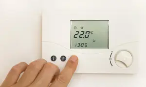 Cyfrowy termostat pokazuje 22.0°C. Dłoń naciska przycisk "F", być może ustawiając temperaturę mieszacza pellet.