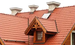 Przegląd instalacji odgromowej na dachu z czerwonej dachówki. Widoczne kominy i okno dachowe.