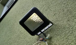 Czarny reflektor LED na zielonej ścianie. Widać, że led świeci po wyłączeniu, prawdopodobnie przez kondensator.