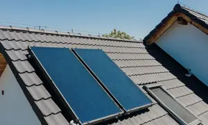 Dwa panele kolektorów słonecznych na szarym dachu, zbierające energię słoneczną.