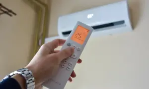 Dłoń trzymająca pilot do klimatyzacji, na ekranie 25°C. Zastanawiasz się, czy klimatyzacja pobiera dużo prądu?