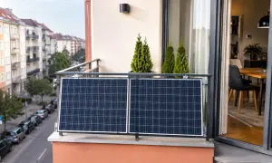 Dwa panele fotowoltaiczne zamontowane na balkonie, obok ozdobnych drzewek. W tle widać ulicę z samochodami i kamienice.