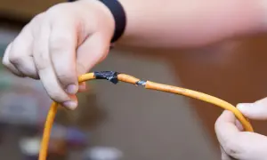 Ręce trzymające przerwany pomarańczowy kabel, pokazując, jak połączyć kable bez lutowania za pomocą taśmy izolacyjnej.