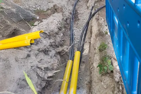 Kable elektryczne w żółtych osłonach w wykopie. Trudno określić na jakiej głębokości kabel elektryczny, ale widać jego zabezpieczenie.