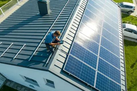 Technik sprawdza, jakie napięcie daje panel fotowoltaiczny, pracując na dachu domu.