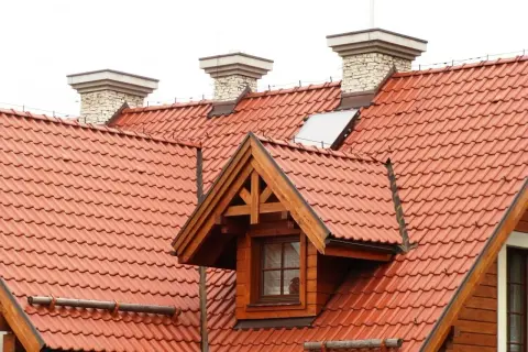 Przegląd instalacji odgromowej na dachu z czerwonej dachówki. Widoczne kominy i okno dachowe.