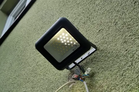Czarny reflektor LED na zielonej ścianie. Widać, że led świeci po wyłączeniu, prawdopodobnie przez kondensator.