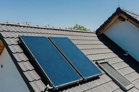 Dwa panele kolektorów słonecznych na szarym dachu, zbierające energię słoneczną.