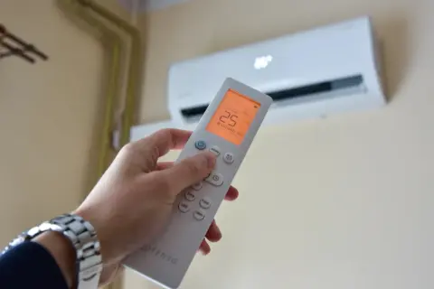 Dłoń trzymająca pilot do klimatyzacji, na ekranie 25°C. Zastanawiasz się, czy klimatyzacja pobiera dużo prądu?