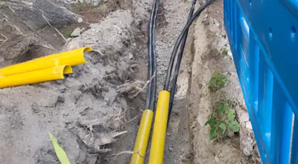 Kable elektryczne w żółtych osłonach w wykopie. Trudno określić na jakiej głębokości kabel elektryczny, ale widać jego zabezpieczenie.
