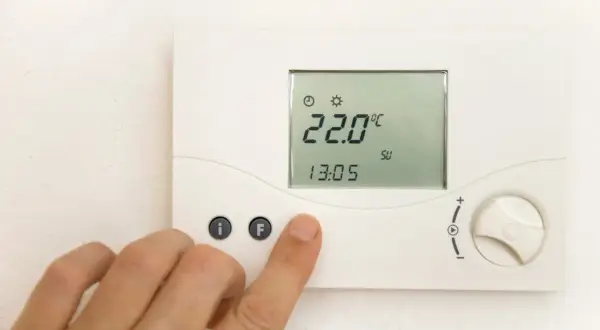 Cyfrowy termostat pokazuje 22.0°C. Dłoń naciska przycisk "F", być może ustawiając temperaturę mieszacza pellet.
