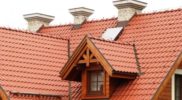 Przegląd instalacji odgromowej na dachu z czerwonej dachówki. Widoczne kominy i okno dachowe.