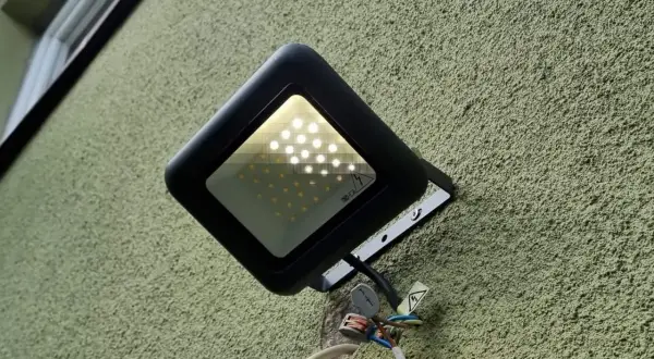 Czarny reflektor LED na zielonej ścianie. Widać, że led świeci po wyłączeniu, prawdopodobnie przez kondensator.