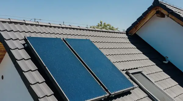 Dwa panele kolektorów słonecznych na szarym dachu, zbierające energię słoneczną.