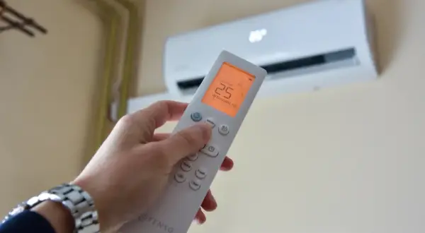 Dłoń trzymająca pilot do klimatyzacji, na ekranie 25°C. Zastanawiasz się, czy klimatyzacja pobiera dużo prądu?