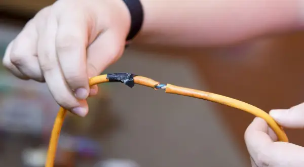 Ręce trzymające przerwany pomarańczowy kabel, pokazując, jak połączyć kable bez lutowania za pomocą taśmy izolacyjnej.