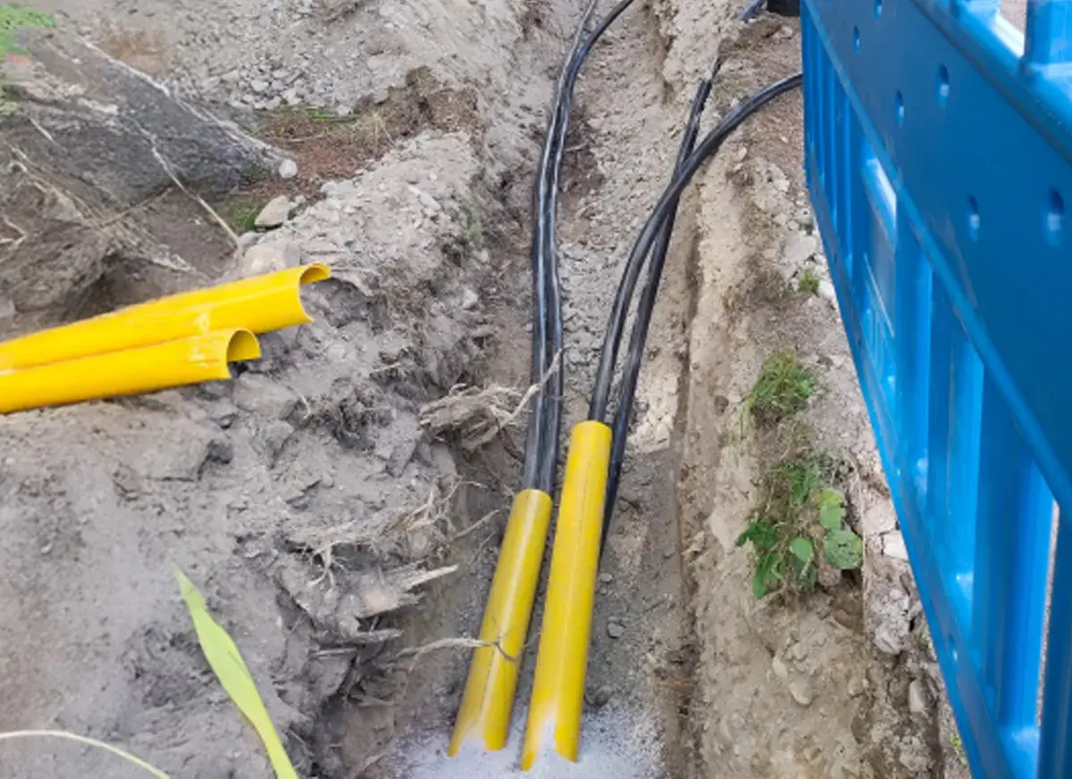 Kable elektryczne w żółtych osłonach w wykopie. Trudno określić na jakiej głębokości kabel elektryczny, ale widać jego zabezpieczenie.