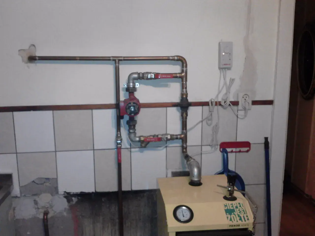 Montaż pompy CO w układzie otwartym. Widoczna instalacja miedziana, czerwona pompa, zawory i fragment kotła.