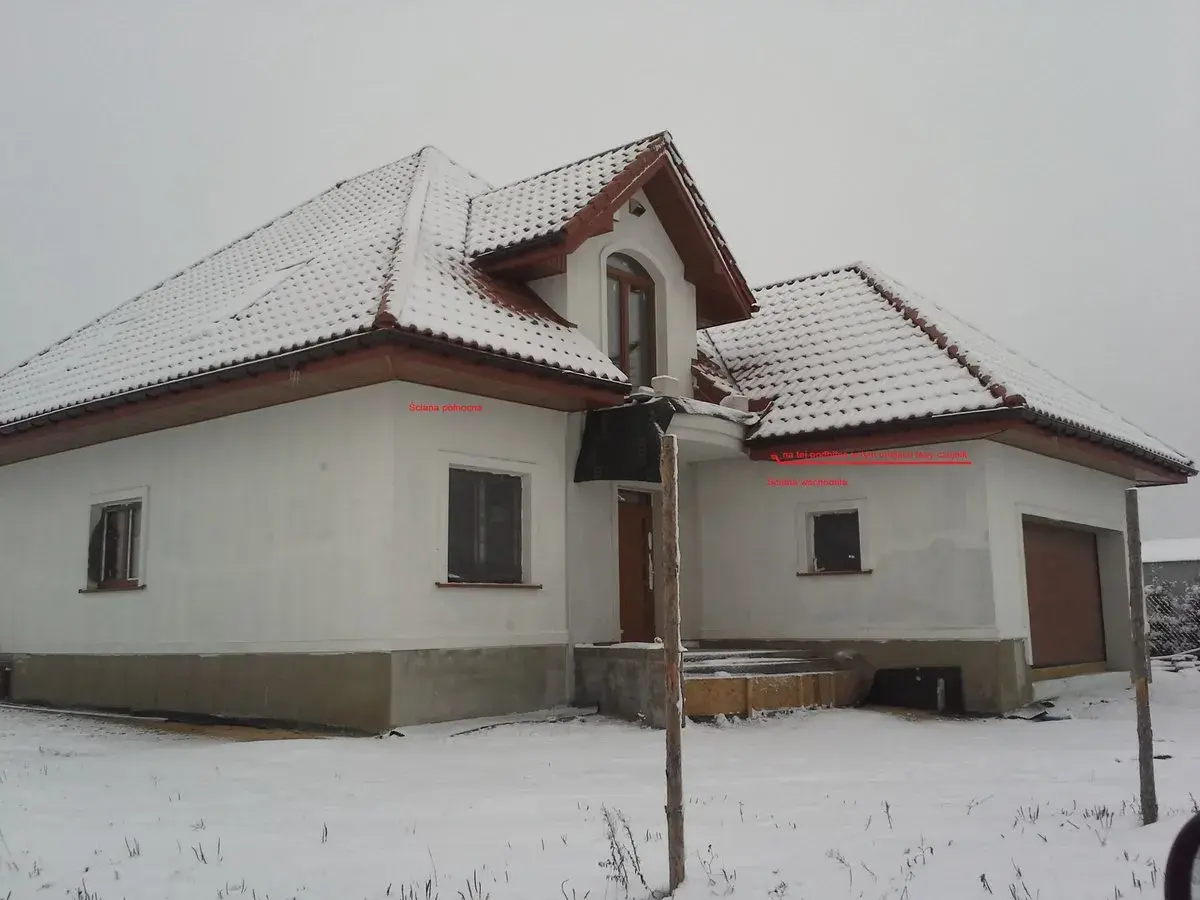 Zimowy dom z ośnieżonym dachem. Na ścianie wschodniej, pod okapem, znajduje się czujnik pogodowy do pieca gazowego, gdzie zamontować go podpowiada strzałka.