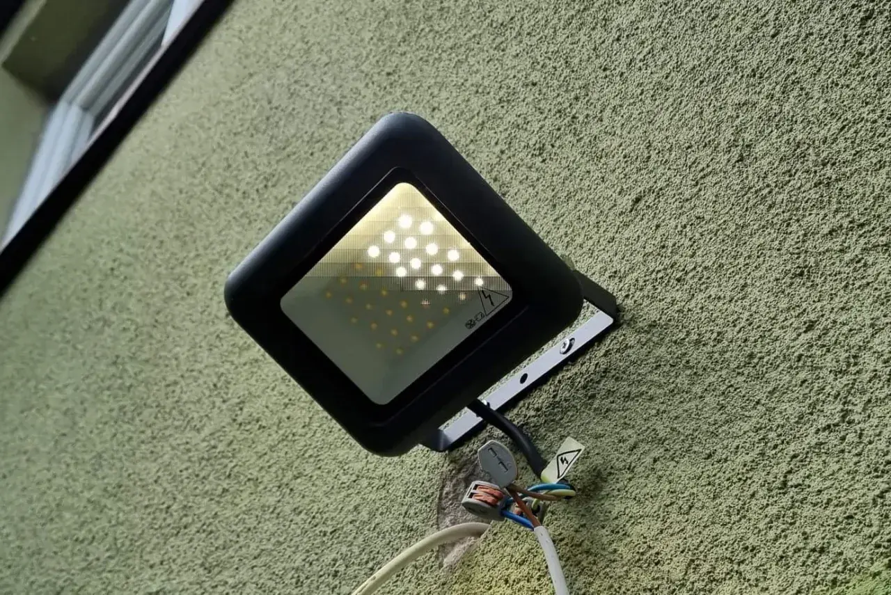 Czarny reflektor LED na zielonej ścianie. Widać, że led świeci po wyłączeniu, prawdopodobnie przez kondensator.
