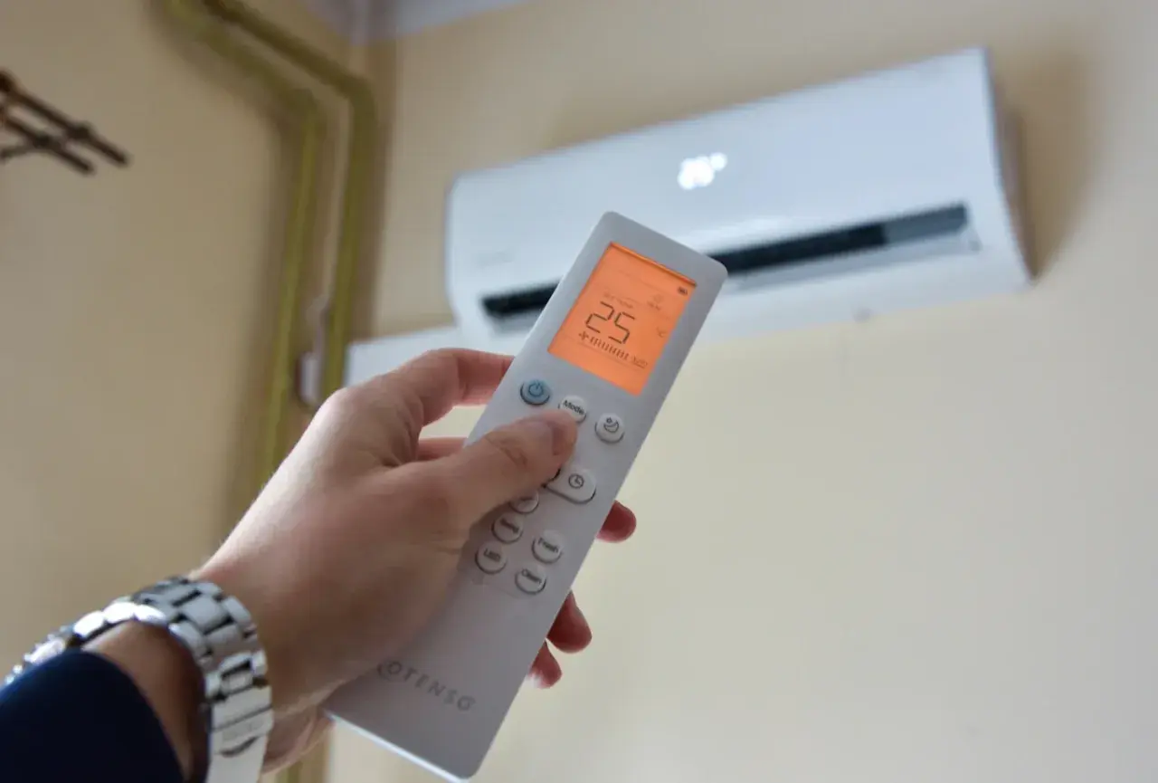 Dłoń trzymająca pilot do klimatyzacji, na ekranie 25°C. Zastanawiasz się, czy klimatyzacja pobiera dużo prądu?