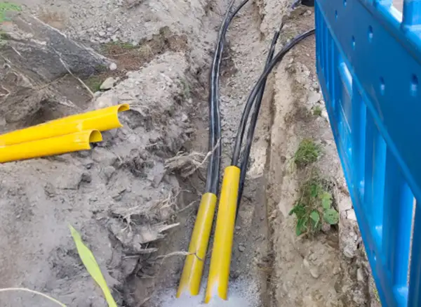 Kable elektryczne w żółtych osłonach w wykopie. Trudno określić na jakiej głębokości kabel elektryczny, ale widać jego zabezpieczenie.