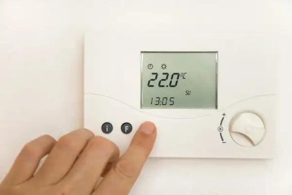 Cyfrowy termostat pokazuje 22.0°C. Dłoń naciska przycisk "F", być może ustawiając temperaturę mieszacza pellet.