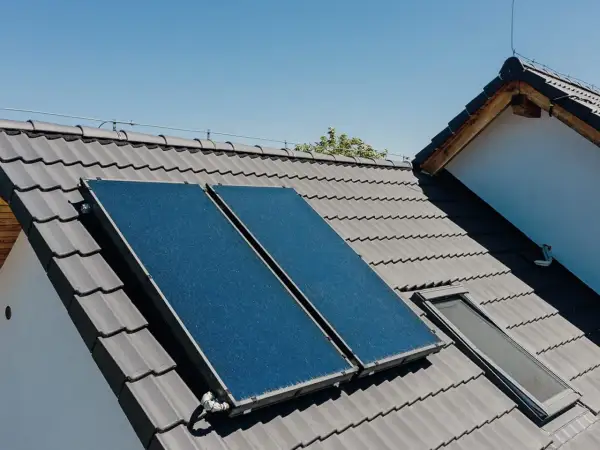 Dwa panele kolektorów słonecznych na szarym dachu, zbierające energię słoneczną.